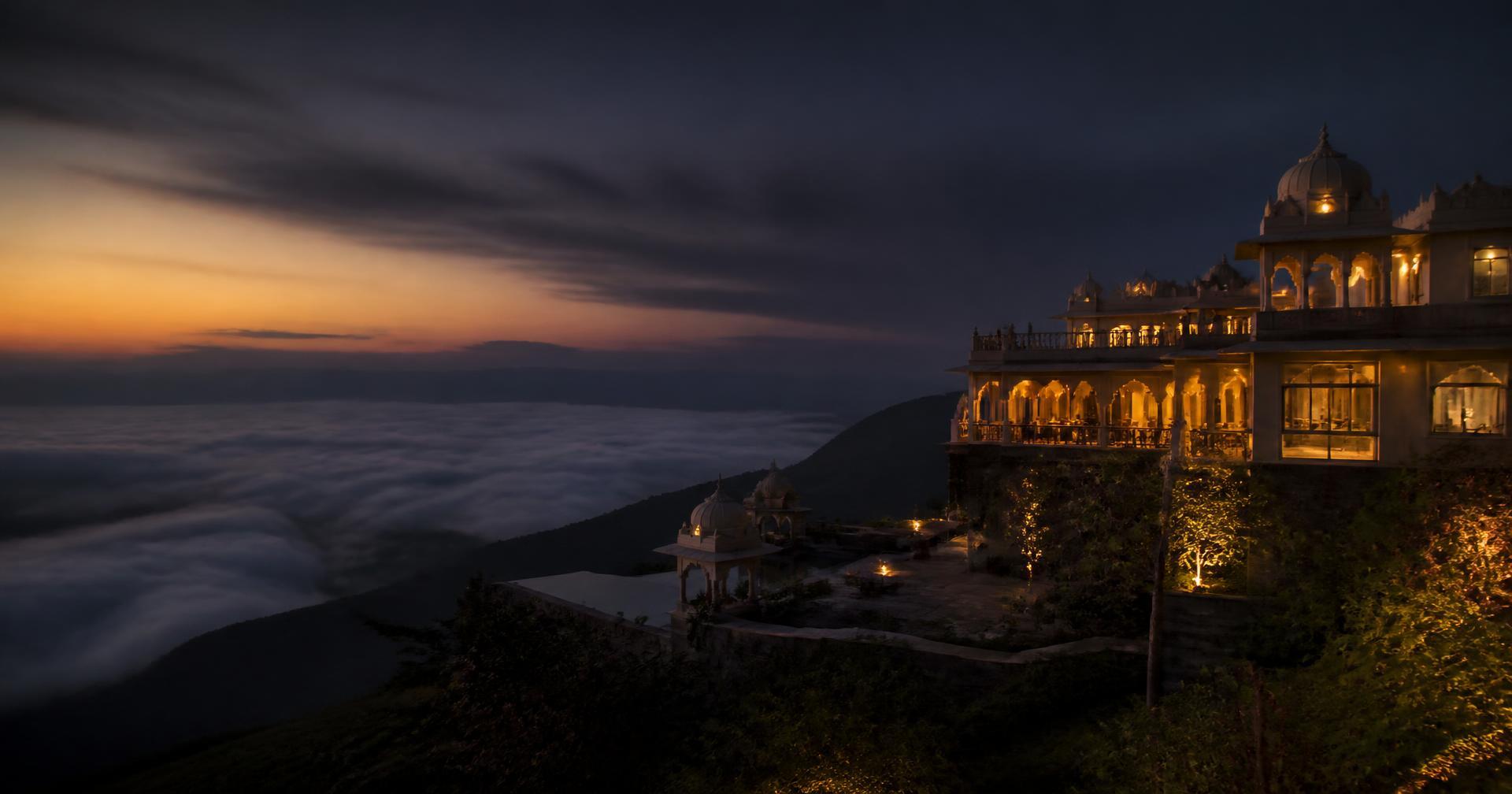 A lit hillside villa above a valley of clouds at dusk